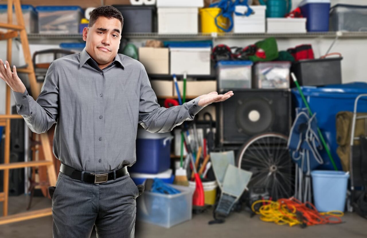 confused man stands in his garage and wonders if he should empty it out